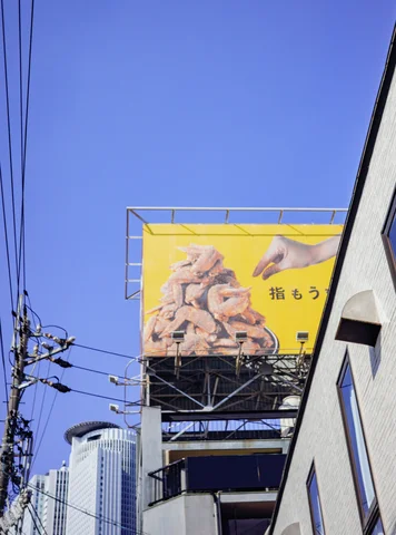 A yellow billboard showing piles of food rises above utility wires beside buildings against a clear blue sky.