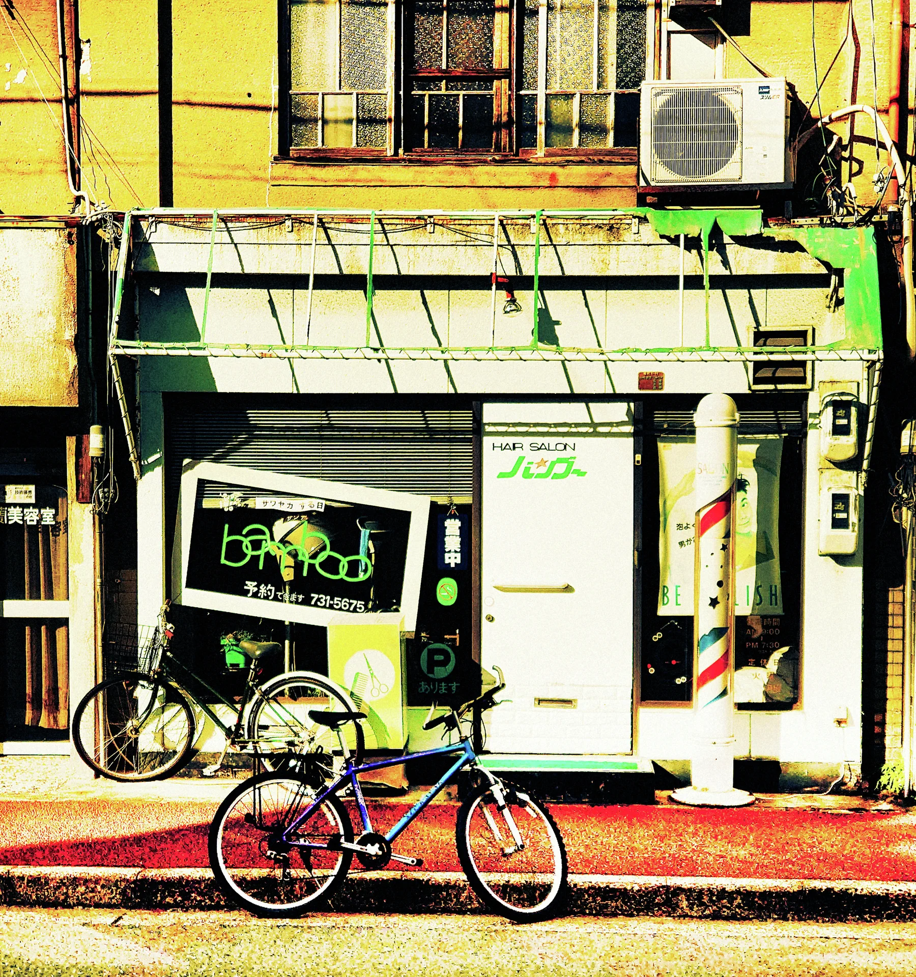Two bicycles stand outside a yellow-toned storefront with a collapsed awning frame and tall white machines.