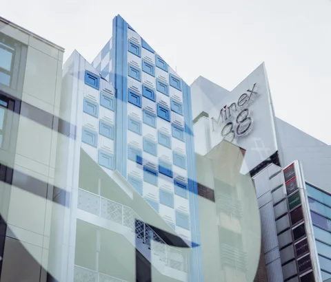 Overlapping reflections show angular pale buildings with blue windows and large rooftop lettering.