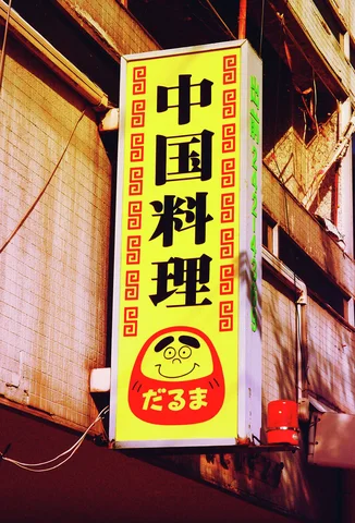 A tall yellow restaurant sign displays black Japanese lettering and a red round cartoon face.