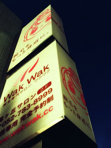 Two stacked pale projecting signs display red Wak Wak lettering against a dark blue sky.