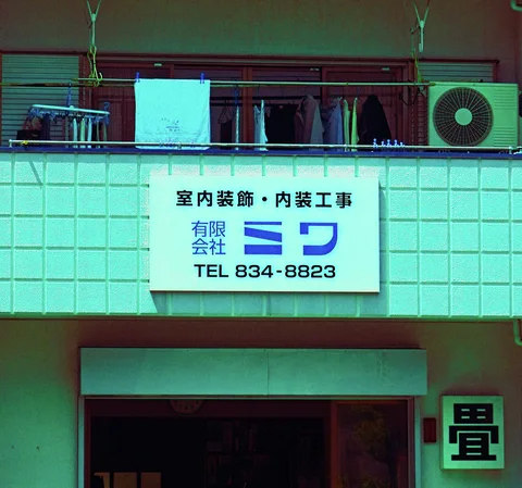 A broad white sign hangs below balcony laundry on a turquoise-toned tiled building.