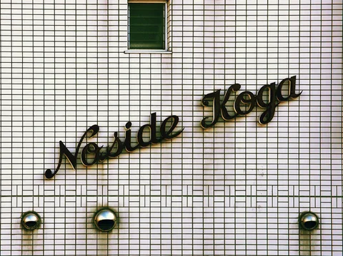 Dark cursive raised lettering crosses a white tiled facade above three small round wall fixtures.