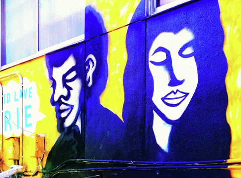 Large stylized blue portraits of a man and woman cover a vivid yellow exterior wall.