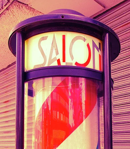 A purple-framed cylindrical salon sign shows stylized lettering above red diagonal stripes and reflected buildings.