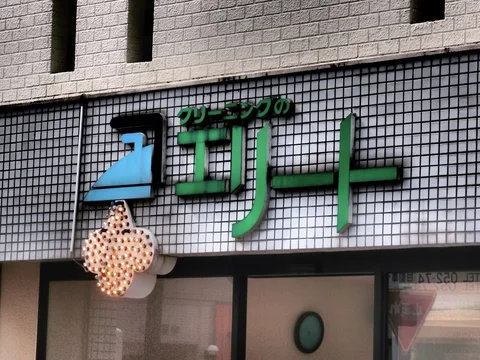 Large green and blue Japanese letters decorate a tiled facade above a glowing cross-shaped ornament.