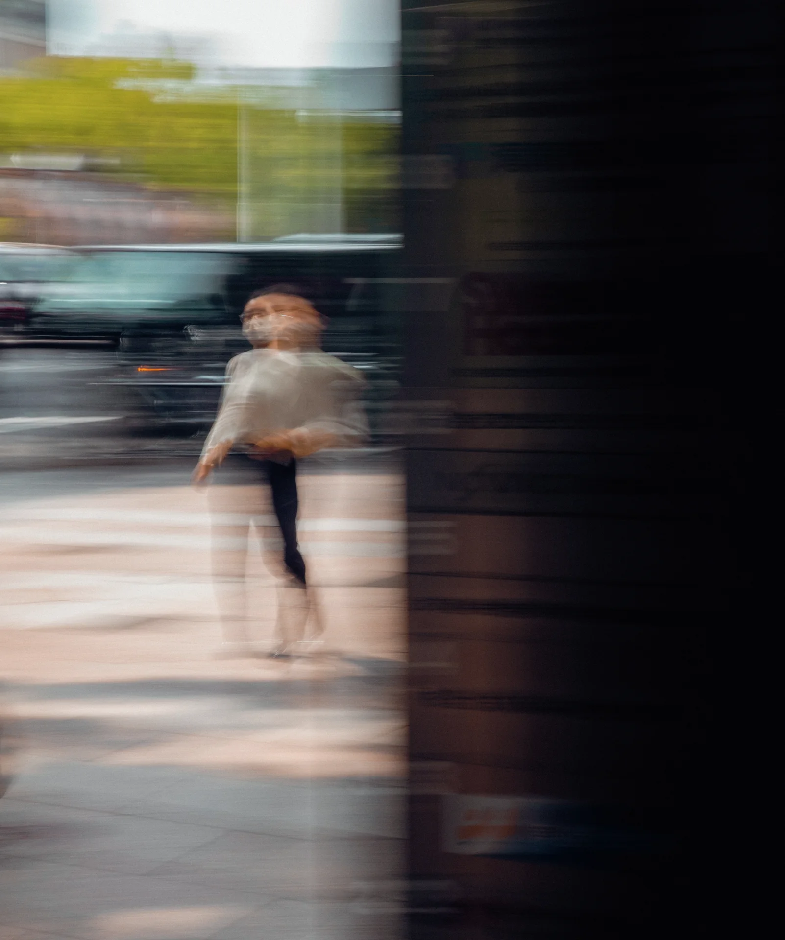 A blurred pedestrian in pale clothing appears beside a broad dark column against streaked street reflections.