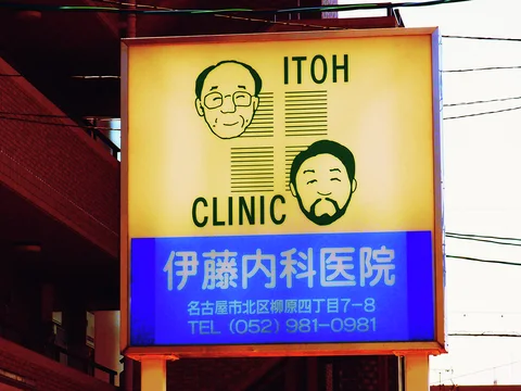 A yellow-and-blue clinic sign displays two cartoon faces beside bold English and Japanese lettering.