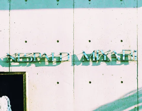 Raised metal lettering casts narrow shadows across a pale concrete wall dotted with circular holes.