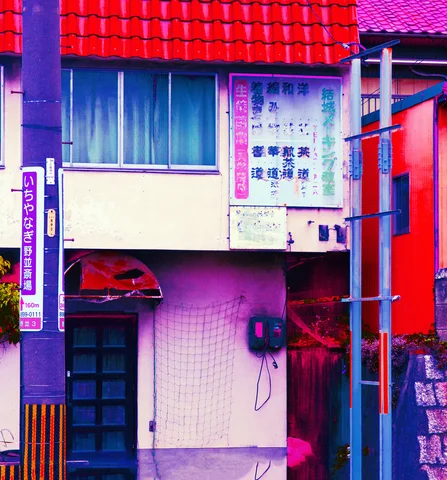 A small tiled facade has a red roof, upper curtained window, and narrow doorway beside a utility pole.
