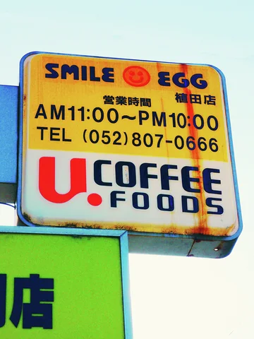 A yellow-and-white projecting cafe sign combines dark lettering, a red smiley face, and stated opening hours.