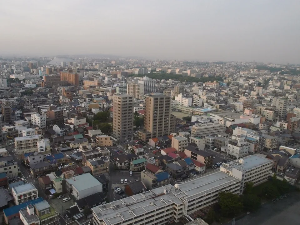 Dense low city buildings and several apartment towers stretch beneath a hazy gray sky.