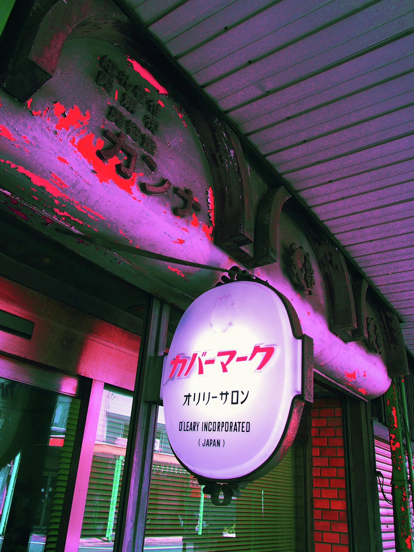 An oval hair salon sign hangs beneath a covered walkway beside a shopfront tinted pink and green.