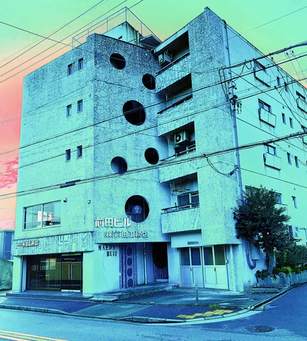 Large circular windows punctuate a pale blue multi-story building beside stacked balconies and overhead wires.