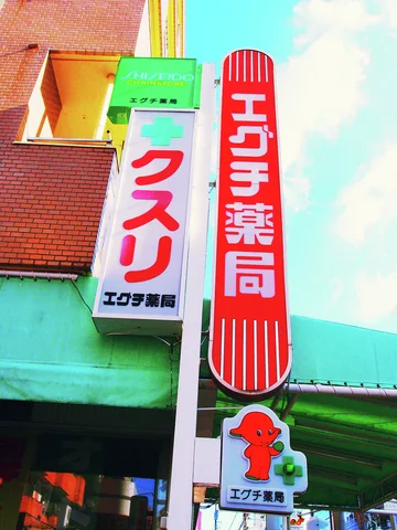 Tall red and white pharmacy signs stand beside a green cross and a small cartoon emblem.