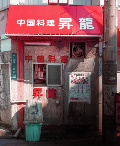 A narrow restaurant entrance has a bright red awning and lettering above its weathered glass door.