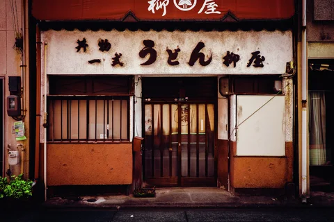 Dark lettering marks a stained cream restaurant sign above a wooden entrance and barred window.
