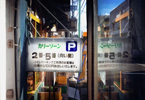 A parking sign hangs beside reflective glass that duplicates a cluttered storefront and outdoor framework.