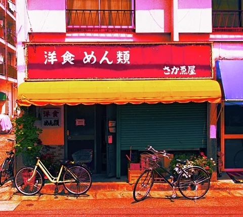 Bicycles stand outside a restaurant beneath a red sign and bright yellow awning.