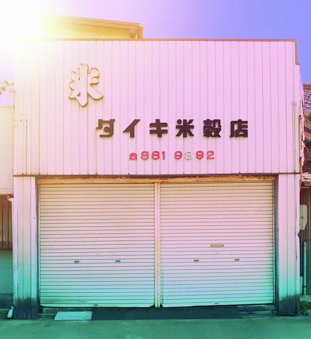 Raised dark lettering and a pale emblem mark a corrugated storefront above two closed shutters.
