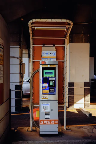 A tall parking payment machine stands beneath a narrow curved canopy beside steps and metal railings.