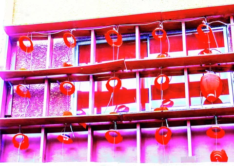 Rows of red hanging lanterns and circular ornaments decorate a gridded window with pink reflections.