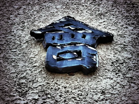 A dark blue raised character casts a shadow against a rough pale stucco wall.