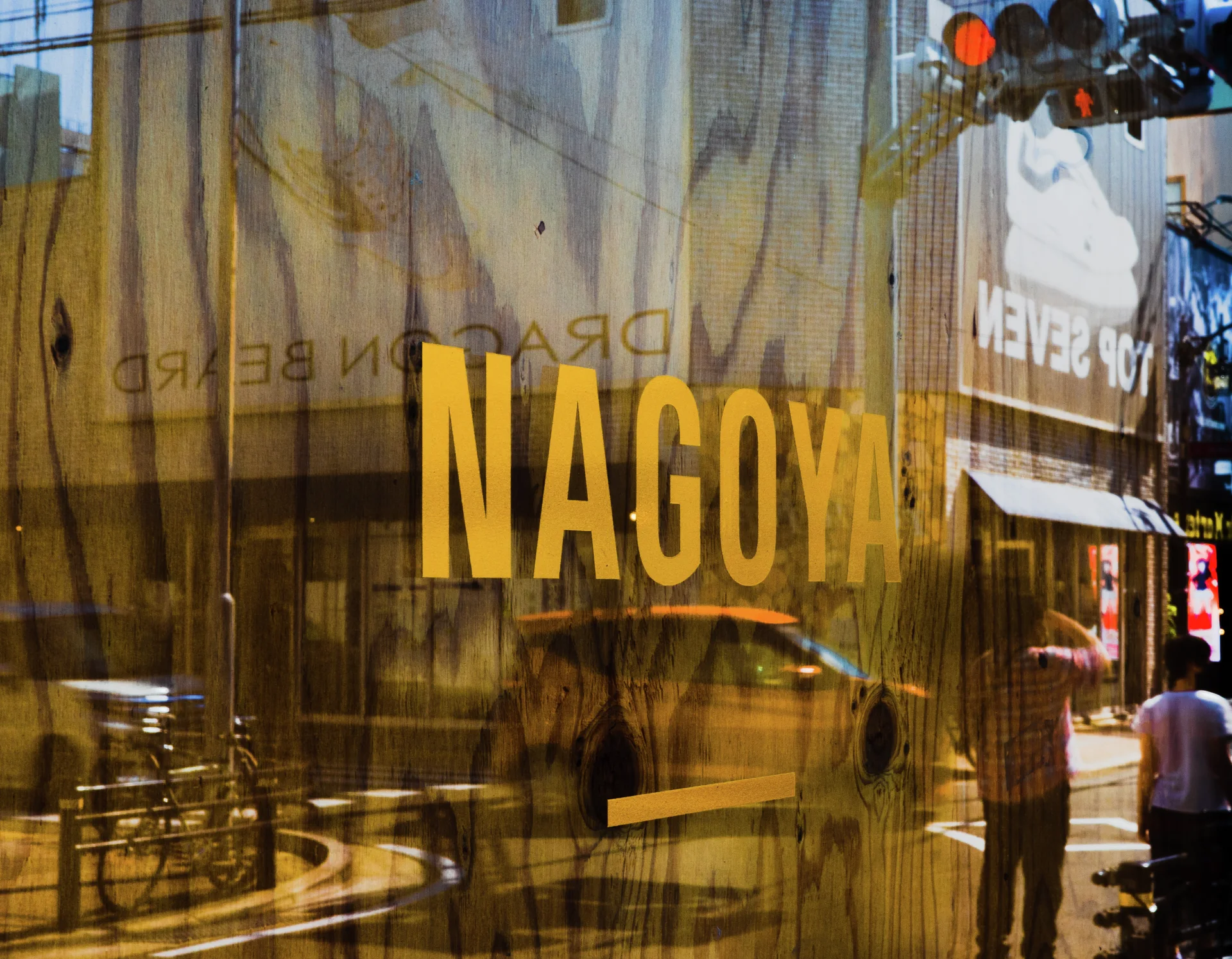 Large yellow NAGOYA lettering appears on reflective glass overlooking bicycles and the street.