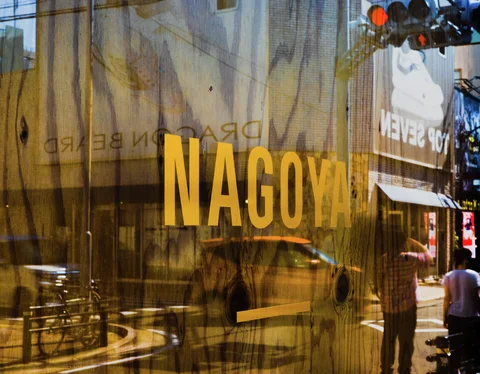 Large yellow NAGOYA lettering appears on reflective glass overlooking bicycles and the street.