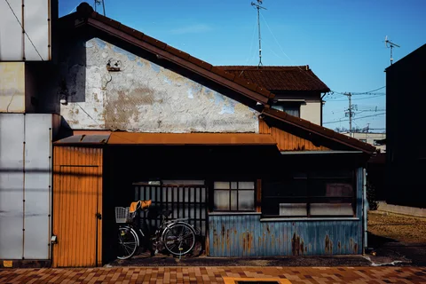 Two bicycles lean against a low weathered building with orange trim and patched pale plaster.