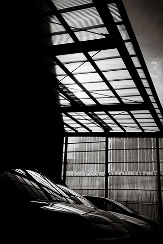 A gridded translucent roof casts geometric patterns above dark stored materials in black and white.
