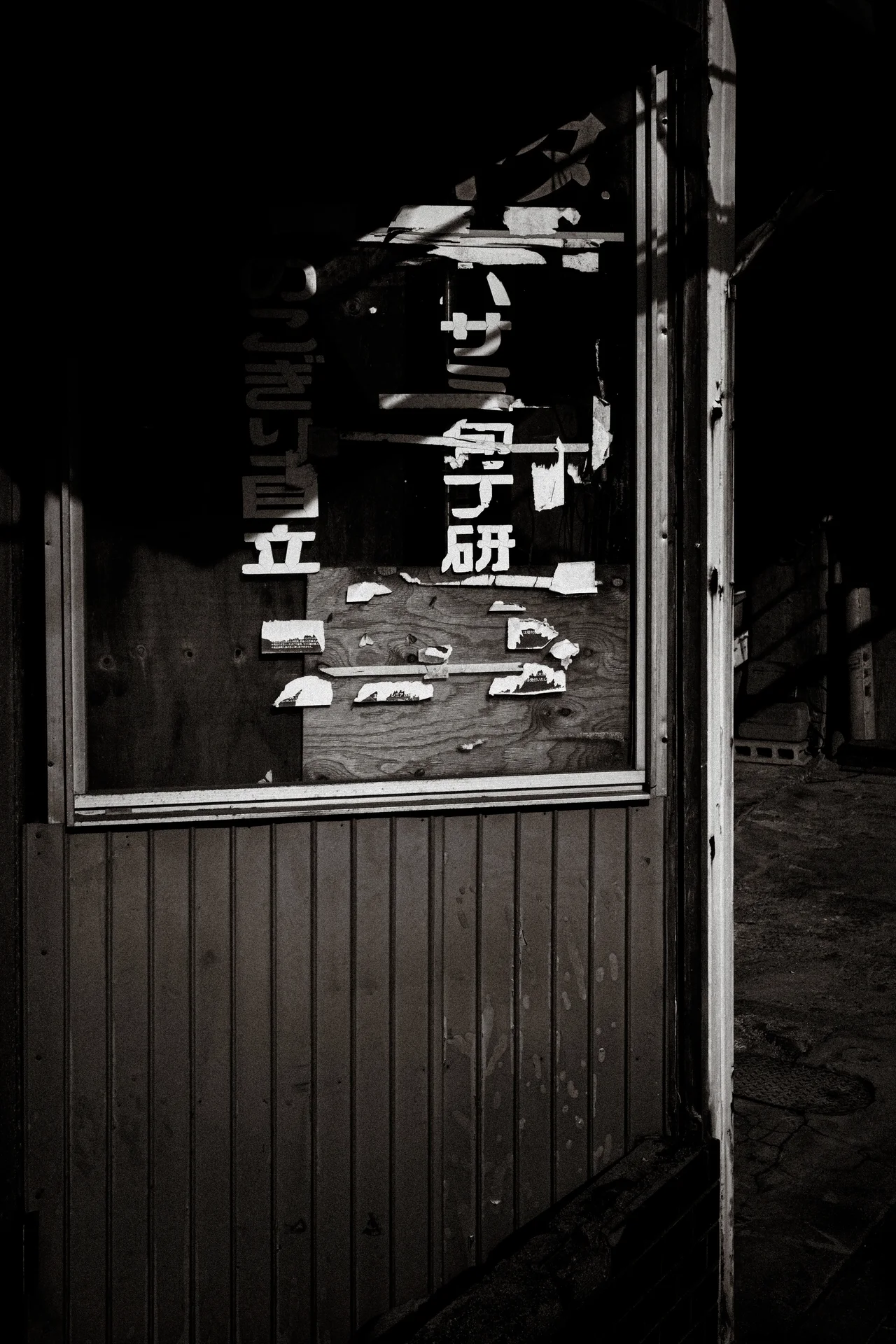 Peeling white characters cover a framed sign on dark wooden siding in monochrome.