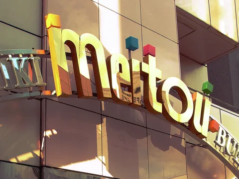 Large pale gold lettering and small colored cubes decorate a sunlit tiled building facade.