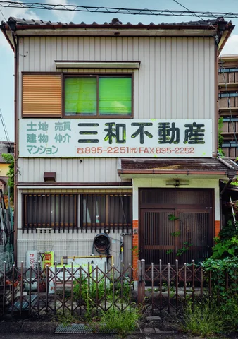 A pale two-story storefront has green window blinds, a large sign, and a fenced frontage.