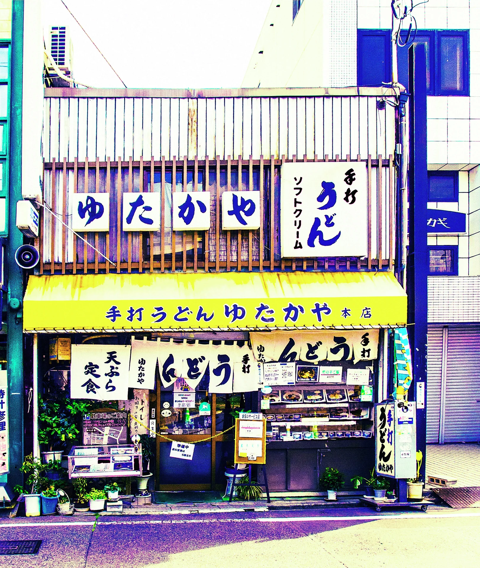 A narrow restaurant facade is covered with signs beneath a yellow awning and barred upper windows.