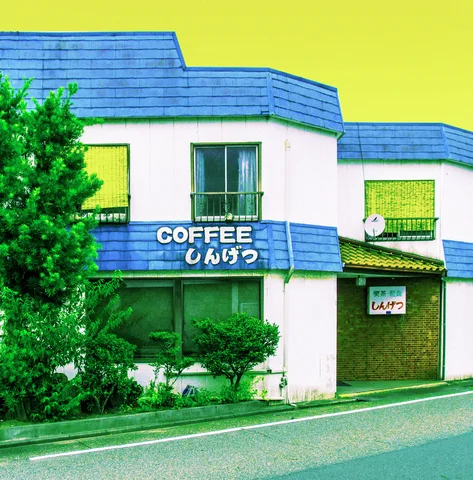 Blue roof trim and white COFFEE lettering decorate a pale corner building bordered by green shrubs.