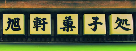 Five yellow square panels display bold dark characters in a row beneath a wooden beam.