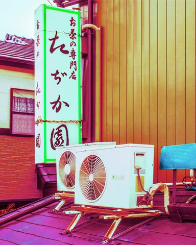 Two outdoor air-conditioning units sit below a vertical Japanese sign beside golden corrugated siding.