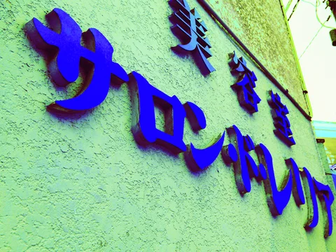 Raised blue salon lettering casts shadows on a textured pale green wall.