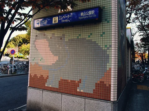 A faded pixel-like tile mosaic decorates a station entrance wall beneath a blue wayfinding sign.