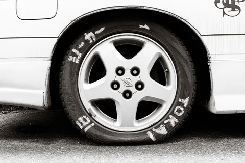 White painted lettering circles a car tire beneath a pale wheel arch in black and white.
