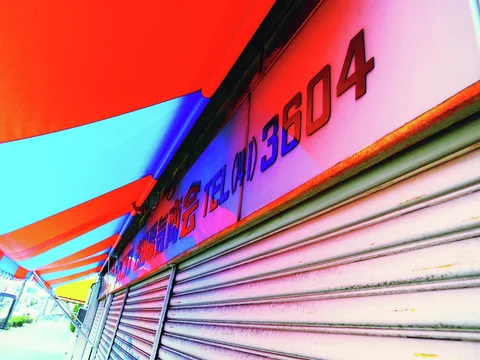 Alternating orange and blue awning bands extend above closed shutters and a long red-lettered sign.