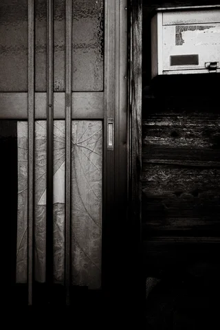 A narrow sliding doorway and weathered wooden panels fill a dark monochrome close-up.