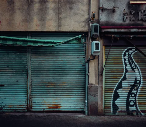 Closed green metal shutters show rusty patches and a large black outlined abstract figure.