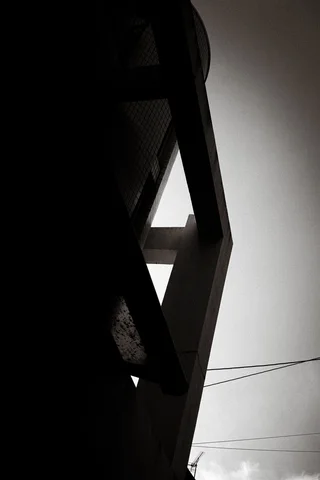A dark angular building edge forms triangular openings against a pale sky crossed by fine wires.