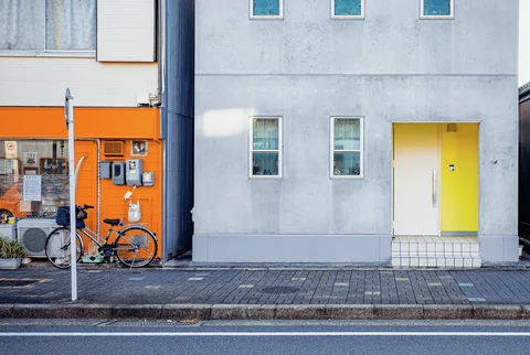 A gray building with a bright yellow doorway adjoins an orange storefront with parked bicycles.