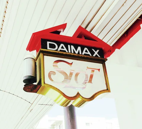A shield-shaped DAIMAX sign with red trim projects from a pale paneled wall.