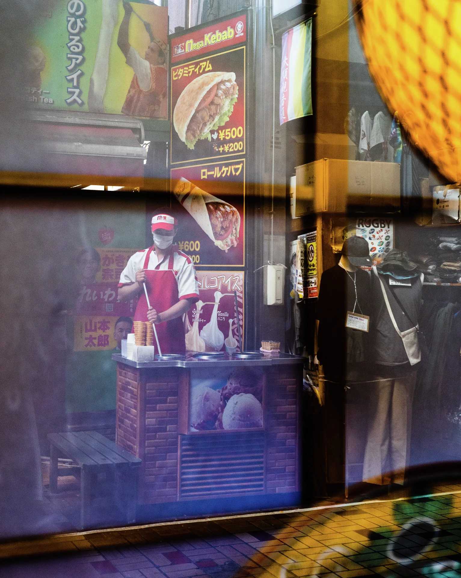 Window reflections overlap a standing figure and food posters beside a yellow patterned panel.
