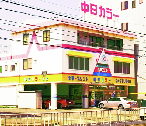 A pale corner building has bright pink trim, yellow awnings, and cars parked beneath its open frontage.