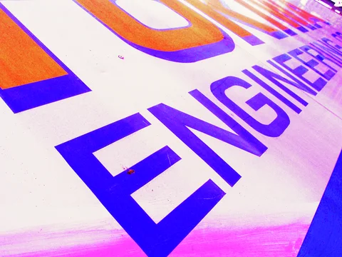 Oversized purple and orange lettering runs diagonally across a brightly colored sign viewed at a steep angle.